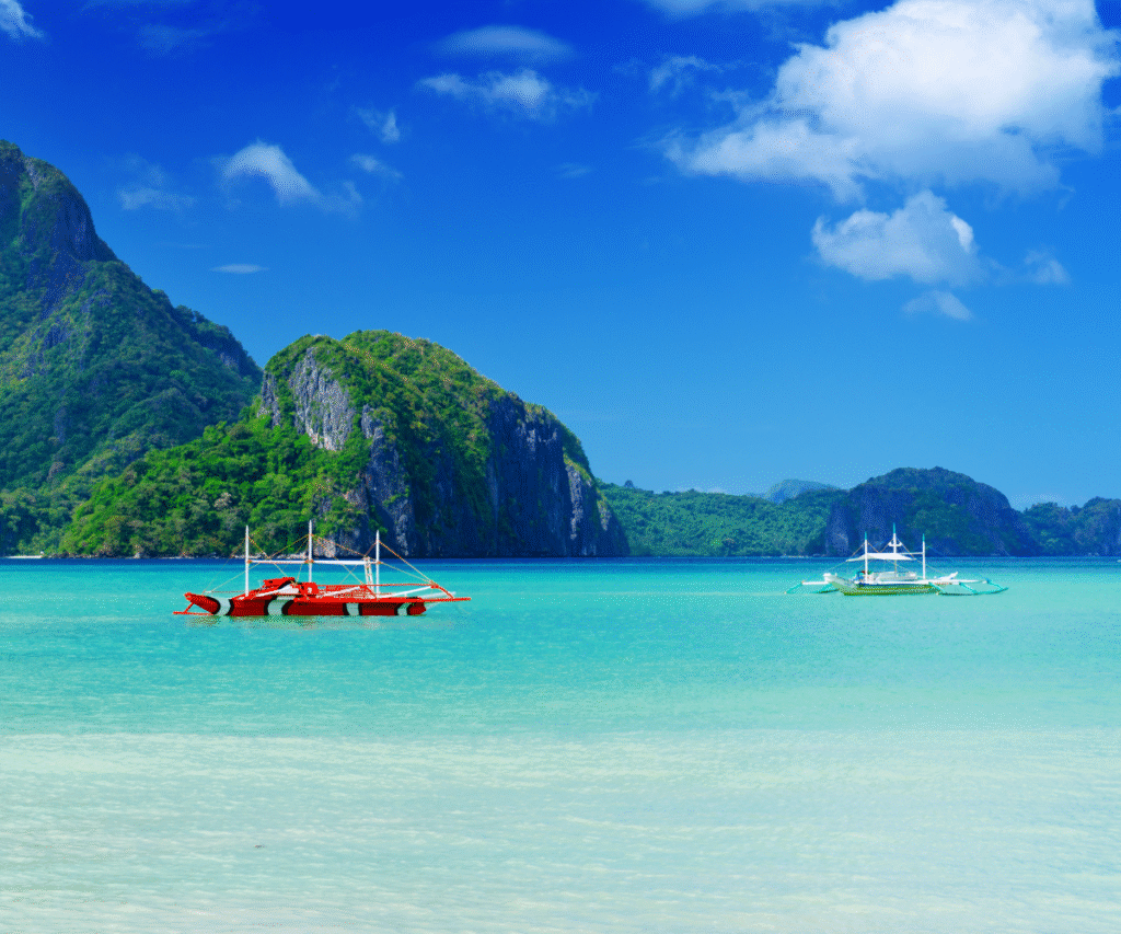 Traditional Filipino boats floating in turquoise water with limestone cliffs in El Nido, Palawan